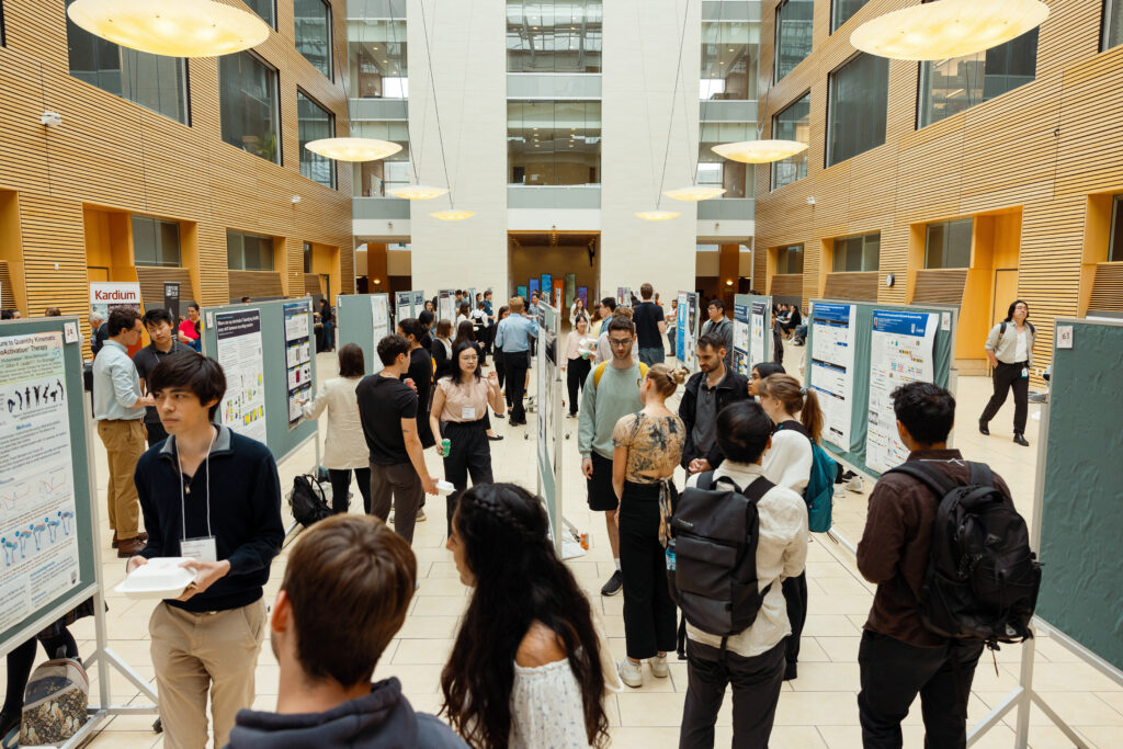 Students standing in the west atrium at LSI on Symposium day looking at posters.